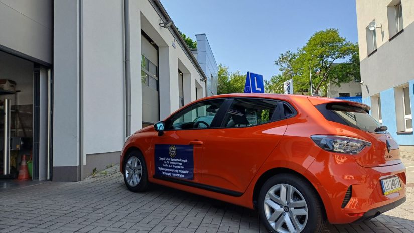 nowy samochód L w kolorze pomarańczowym stoi na placu warsztatowym przed stacją kontroli pojazdów