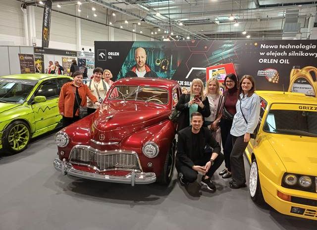 grupa nauczycieli ZSS podczas Warsaw Motor Show, stoją na tle jednego ze stoisk przy odrestaurowanej Warszawie